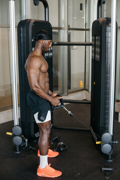 Strong man using cable machine for triceps workout. Fit African American athlete performing triceps pushdown with rope attachment on gym cable machine during workout.