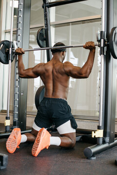 Muscular man performing lat pulldown on smith machine in gym. Strong athletic man training back muscles with bar on gym machine.