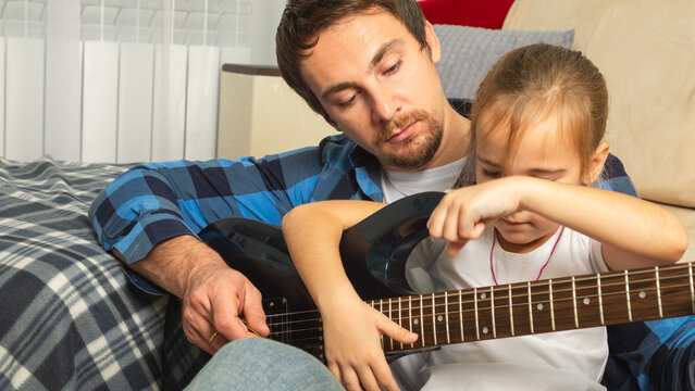 Dad teaches daughter to play guitar in living room. Dad and daughter spend time together. - Powered by Adobe