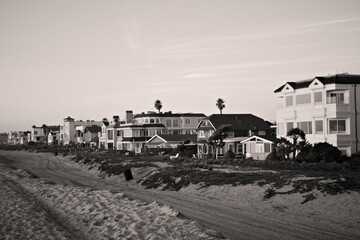 Beachfront homes line a sandy shoreline at golden hour in Sunset Beach, California, with warm light, pastel sky, and calm coastal atmosphere.