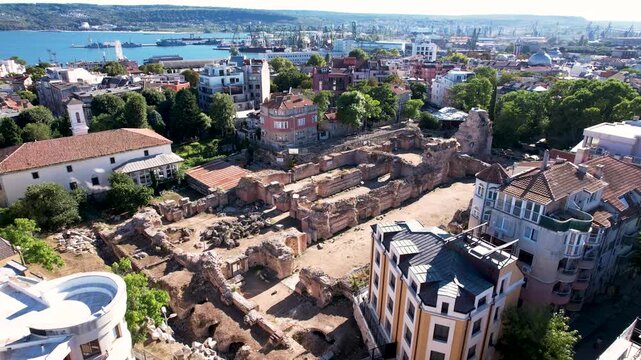 Aerial view of the ancient Roman Thermae ruins standing amidst the modern city, contrasting old stone with vibrant buildings, Varna, Varna, Bulgaria.