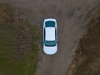 A white car parked on a dirt road, photographed from a aerial view for a unique angle.