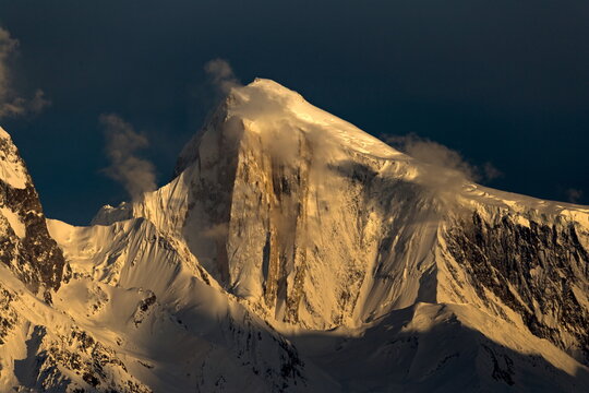 View of a majestic mountain peak, draped in snow and touched by golden light, against a deep blue sky in Hunza, Gilgit Baltistan, Pakistan.