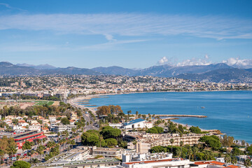 Obraz premium Panoramic coastal city view with blue sea, urban shoreline and distant mountains under clear sky