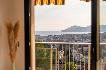 Fototapeta premium City and mountain view from apartment balcony through open window in warm evening light