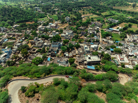 Aerial view of a vibrant tapestry of rooftops nestled amidst lush greenery, winding roads, and verdant hills, Mangar, Haryana, India.
