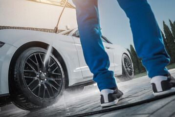 Person Washes Car Wheels at a Driveway on a Sunny Day