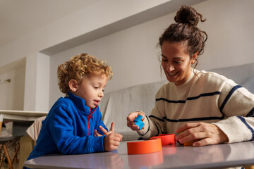 Happy mother and young son engaging in playful learning, collaborating and developing skills with building blocks at a table
