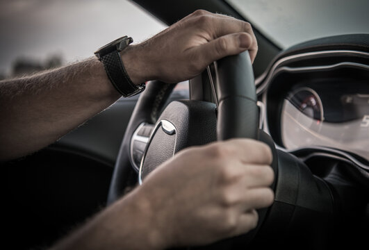 Driver Holds Steering Wheel While Driving on a Road in Daylight