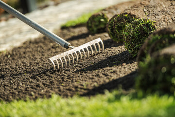 Raking Soil Before Laying Sod in a Backyard on a Sunny Afternoon