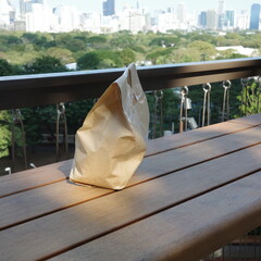 Takeaway paper bag on wooden table with city park and skyline in background.