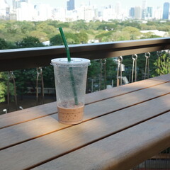 Iced coffee cup on wooden table overlooking city park with urban skyline view