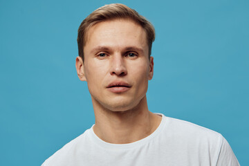 Fototapeta premium Close up serious young caucasian man wearing white t-shirt look camera isolated on light blue background mental health and gadgets concept portrait.