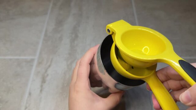 Female hands squeeze fresh lime juice using a citrus press into a metal cocktail shaker. Minimal overhead view capturing a complete beverage preparation action.