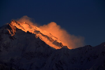 View of a majestic, snow-capped mountain peak ablaze with golden light against a deep blue sky, creating a stunning contrast of warmth and cold, Passu, Gilgit Baltistan, Pakistan.