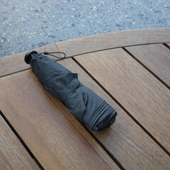 Folded black umbrella resting on wooden table outdoors 