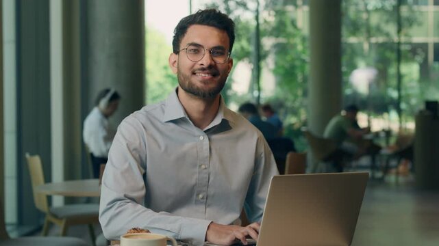 Indian businessman working with laptop technology Arabian ethnic business man using computer cyberspace network indoors in coworking office smiling looking at camera Muslim guy employer work online