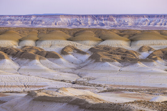 View of the textured, layered earth, sculpted by time and weather, showcasing the arid beauty under a soft twilight sky, Senek, Mangystau Region, Kazakhstan.