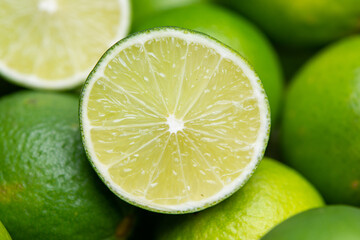 Close-up of a fresh lime cut in half, revealing its juicy, textured interior, surrounded by whole limes and vibrant green leaves.