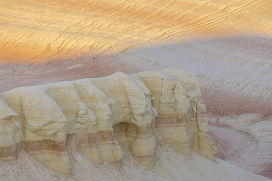 View of stark white and red rock formations under a sky of soft peach and orange, textured and striated, in Senek, Mangystau Region, Kazakhstan.