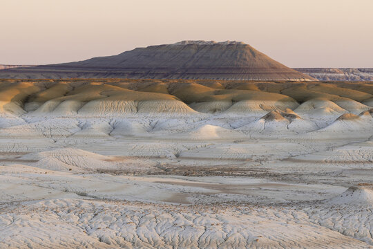 View of textured sedimentary rock formations under a soft sky, creating a landscape of layered earth tones and subtle shadows, Senek, Mangystau Region, Kazakhstan.