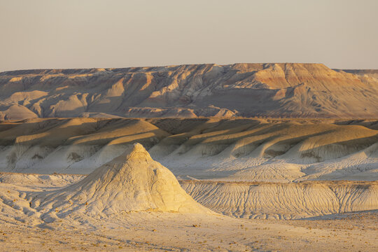 View of sun-kissed desert mounds rise from the arid landscape, a symphony of beige and brown under a pale sky, Senek, Mangystau Region, Kazakhstan.
