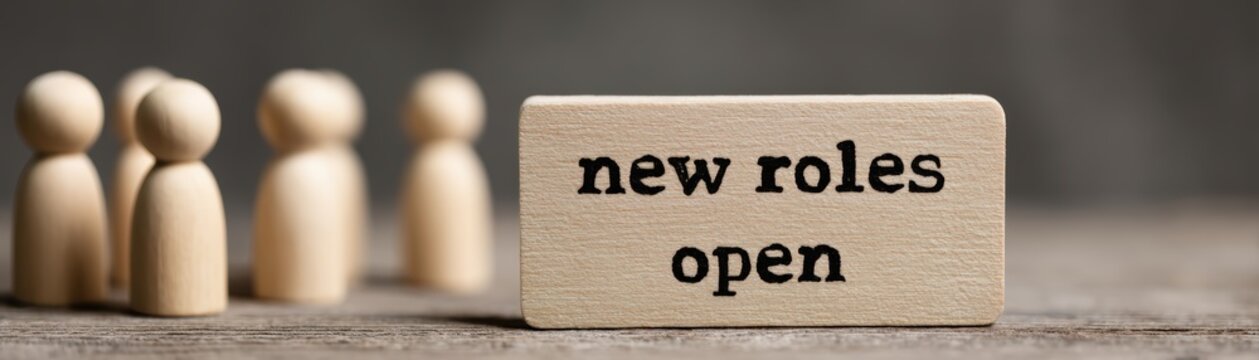 A wooden block displays "new roles open" with wooden figures in the background, symbolizing job opportunities and recruitment, HR work announcement