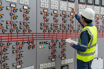 An electrical engineer in a hard hat and safety vest inspecting a control panel board in a power station control room. Technical monitoring of energy distribution and electrical systems management. © JD Studio
