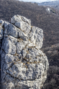 View of weathered limestone formations rise majestically against a backdrop of hills and sparse trees, their textures contrasting with the soft sky, Buda Hills, Hungary.