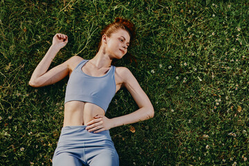 Young athletic woman in blue activewear lying on green grass, demonstrating relaxation and tranquility in a natural setting