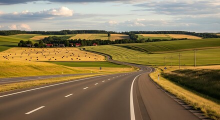 A winding highway gracefully cuts through a vibrant countryside scene, surrounded by rolling green hills and harvested fields under a cloudy sky