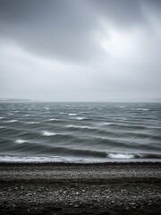 A gray and cloudy beach with choppy waves and a rocky shoreline.
