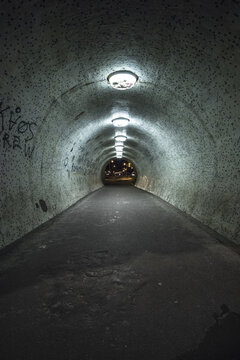 View of a long, dark tunnel illuminated by evenly spaced lights, creating a sense of depth and mystery, leading to a bright exit, Budapest, Hungary.