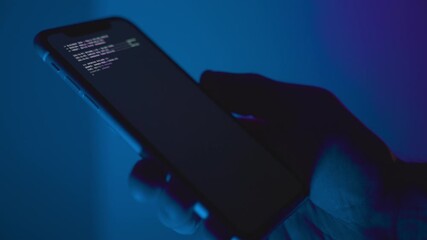 Hand holding smart phone on dark blue background while malware app is installed. Close up on device hacking code running on screen downloading and setup of illegal criminal spyware cybersecurity virus - Powered by Adobe