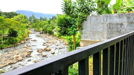 A lush tropical river landscape flowing through a green rural valley, surrounded by dense trees, farmland, and misty mountains, capturing natural serenity and countryside life
