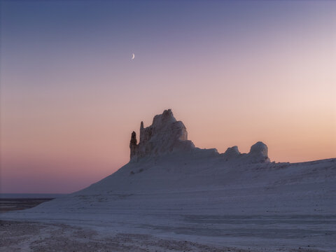Aerial view of the stark white rock formations under a pastel sky, with a sliver of moon hanging above, Bozhira, Mangystau Region, Kazakhstan.