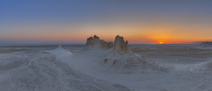 Aerial view of the chalky landscape and rock formations as the sun rises, casting a warm glow across the horizon, Bozhira, Mangystau Region, Kazakhstan.