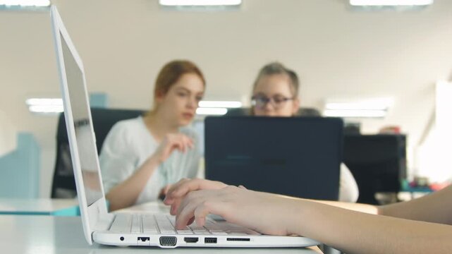 Teacher and students studying and working on laptops in modern classroom computer lab, rack focus from hands to portrait