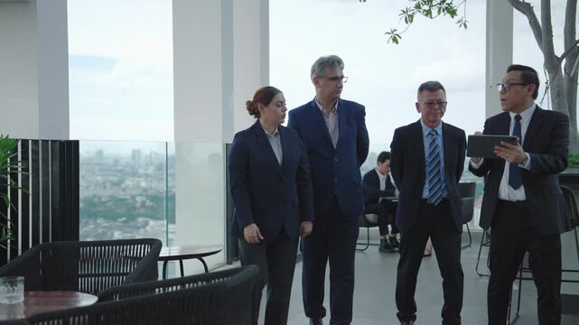 Diverse business team walking together on rooftop terrace while discussing work and using digital tablet. Concept of leadership, teamwork, strategy, and corporate collaboration.
