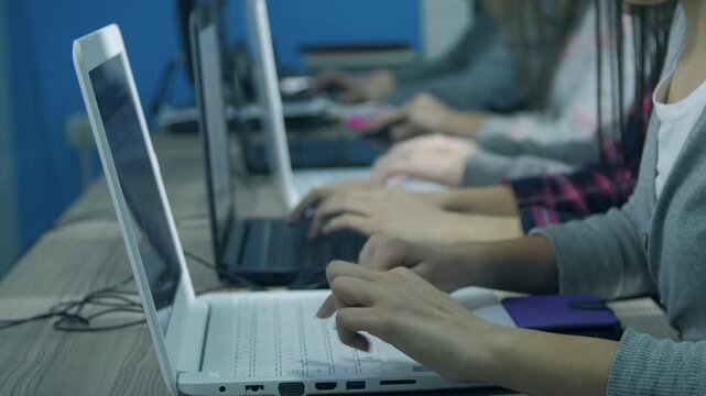 Children hands typing on keyboards of four laptops with rack focus effect, digital education concept