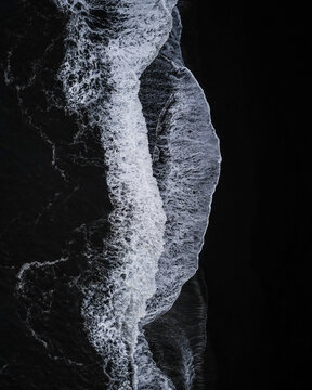 Aerial view of the dramatic meeting of frothy white waves and stark black sands creates a mesmerizing contrast at the shoreline, Vik, Western Region, Iceland.