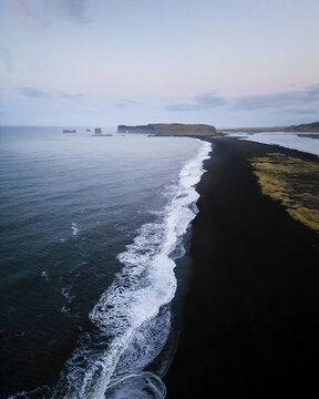 Aerial view of the stark contrast between the obsidian sands and the turquoise waves meeting the horizon near Dyrh&oacute;laey, Vik, Western Region, Iceland.