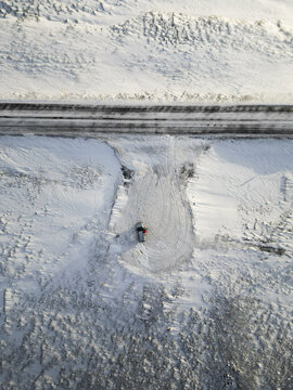 Aerial view of a solitary figure stands amidst a snow-covered expanse, a stark contrast to the dark road above, in a winter wonderland, Vik, Western Region, Iceland.