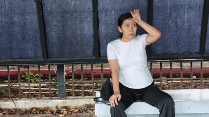 A tired pregnant woman sitting at a modern city bus shelter, looking exhausted while waiting for public transport
