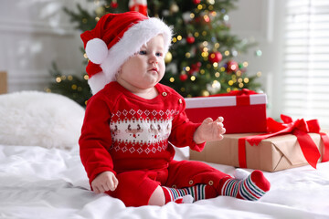 Cute little baby in Santa hat and gift boxes on bed at home. Christmas season