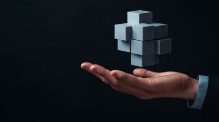 A hand holds a floating, geometric structure, symbolizing innovation and technology in a dark, minimalist background.