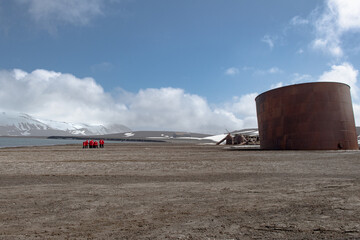 View of a rusty cylindrical tank standing sentinel on the barren, snow-dusted landscape against the backdrop of distant mountains, Deception Island, Antarctica.