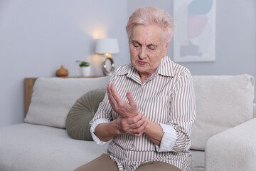 Senior woman suffering from wrist pain at home, space for text. Rheumatism symptom