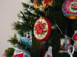 A close-up shot of handmade cross stitched Christmas ornaments featuring an embroidered poinsettia design hanging on a Christmas tree. All Christmas ornaments embroidered and made by myself.