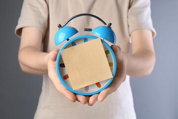 Woman with sticky note and alarm clock on light grey background, closeup